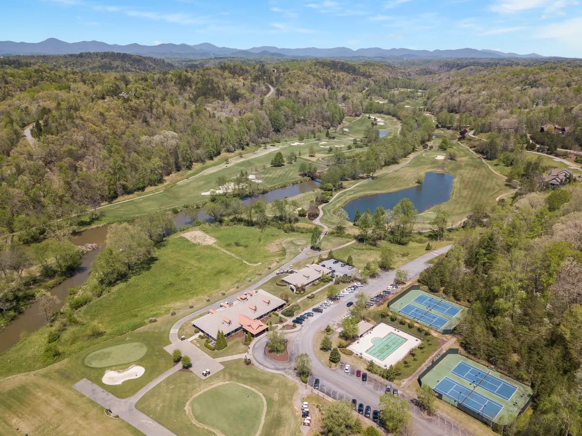 Aerial view of a golf course with fairways, sand bunkers, ponds, tennis courts, and forested mountain ridges