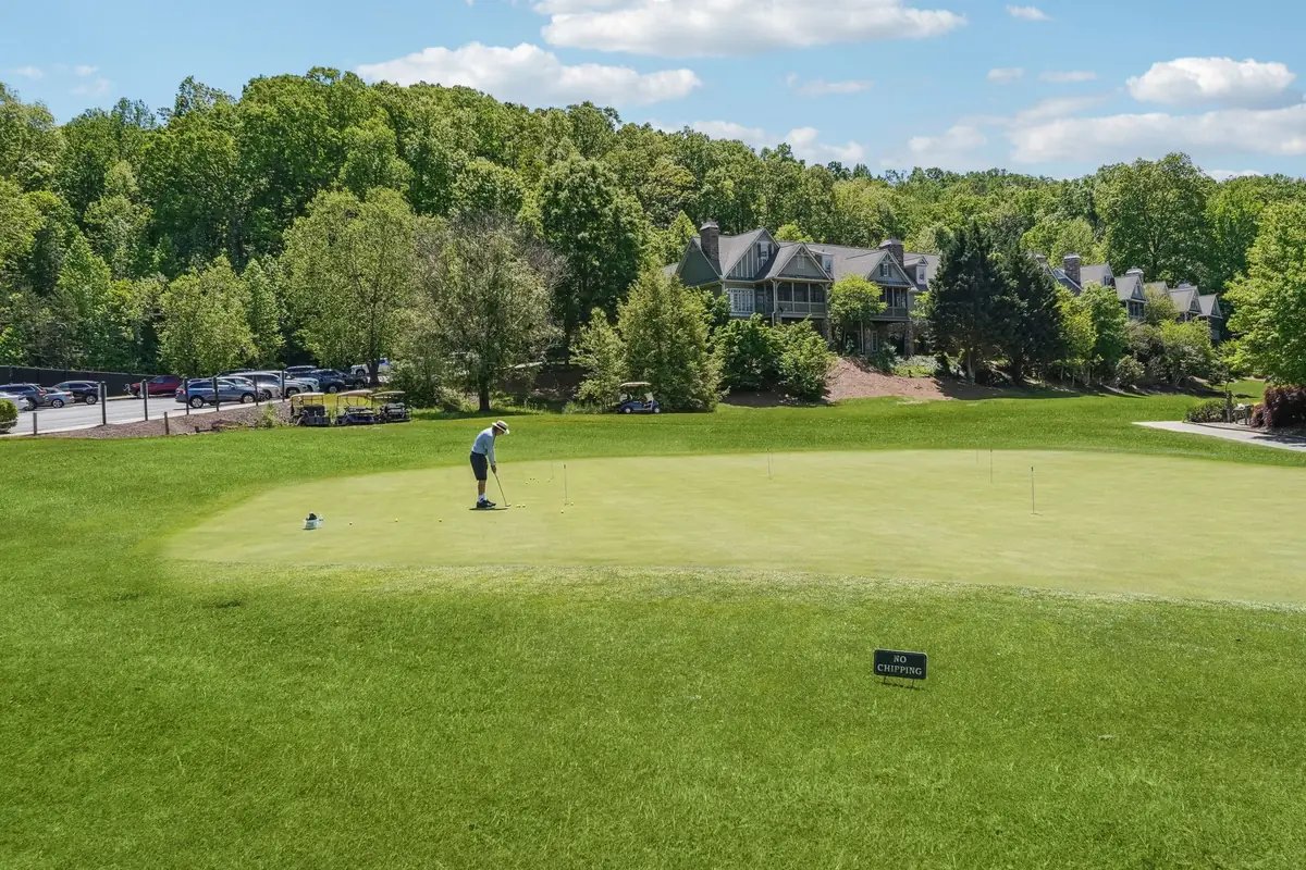 Golfer on a putting green with homes and wooded hills beyond